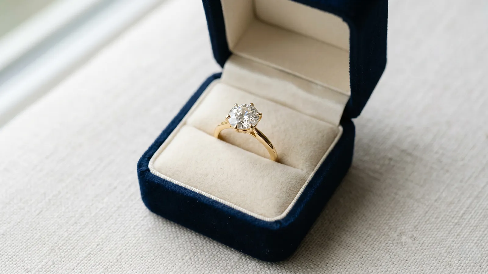 Open jewelry box revealing an engagement ring in a softly-lit setting